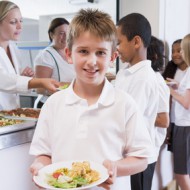 Schoolboy holding plate of lunch in school cafeteria